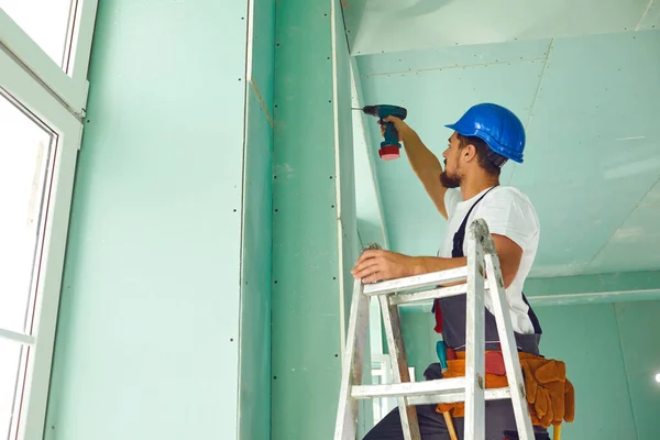 Ein auf einer Leiter stehender Bauarbeiter installiert Trockenbau auf einer Baustelle — Stockfoto