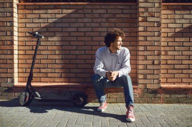 Kasklı genç adam yazın bir şehir caddesinde elektrikli scooter kullanıyor.