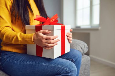 Kırmızı kurdeleli, hediye kutulu mutlu kız odada oturuyor..