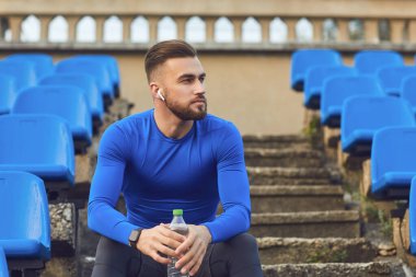 Spor giyimli bir adam antrenmandan sonra stadyumda oturuyor..