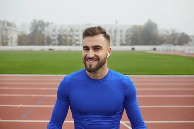 Mavi elbiseli bir sporcu siste stadyuma bakarken gülümsüyor.