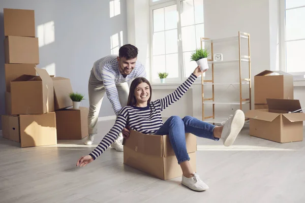 Een vrolijk stel speelt met een verhuisdoos in een lichte kamer van een nieuw huis. — Stockfoto