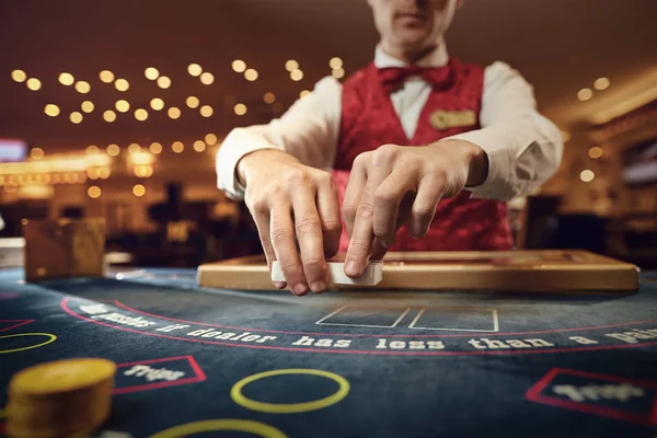 Croupier trzyma w rękach karty pokerowe przy stole w kasynie. — Zdjęcie stockowe