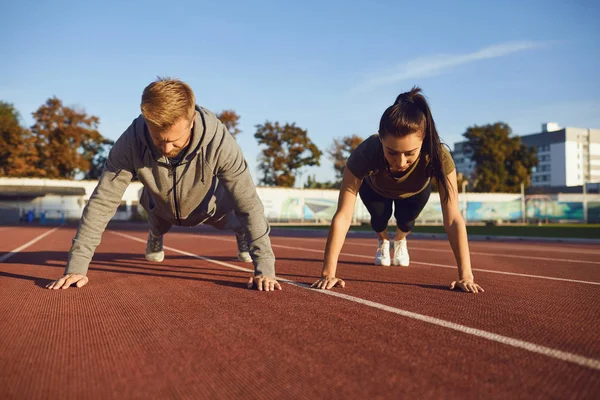 Young couple doing pushups in the stadium — Stock Photo, Image