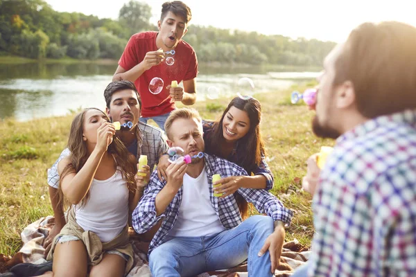 Young people make soap bubbles while sitting on the grass on in nature.