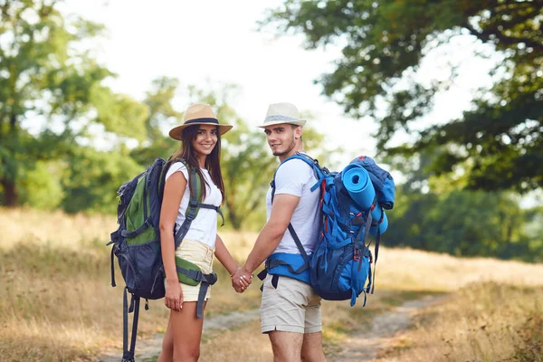 Happy couple of travelers with backpacks hold hands on nature — ストック写真