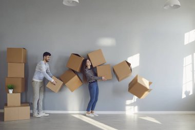 Happy funny couple holds cardboard boxes for moving in new apartment house room