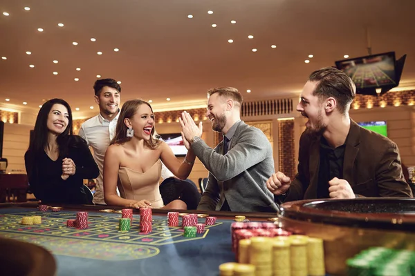 Cheerful group of friends enjoys winning poker roulette in a casino. — ストック写真