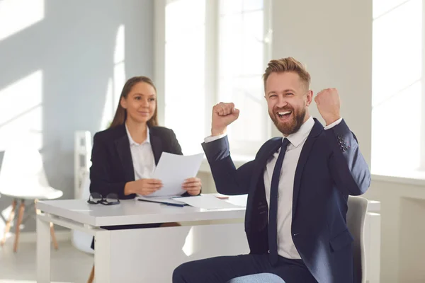 Successful interview. A man in a suit rejoices at a new job sitting at a table with a woman employer in a white office. — Stock Photo, Image