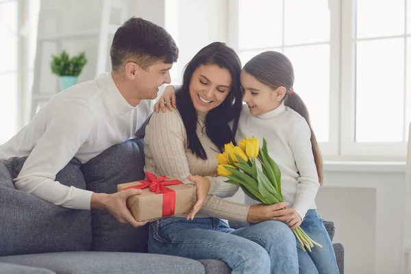 Gelukkige Moederdag. Vader en baby dochter feliciteert moeder met bloemen en een ansichtkaart in een kamer — Stockfoto