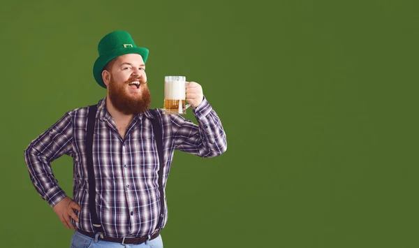 Feliz dia de St. Patricks. Gordo em um chapéu verde mantém as mãos erguidas óculos com cerveja — Fotografia de Stock