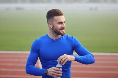 Spor giyimli bir adam antrenmandan sonra stadyumda oturuyor..