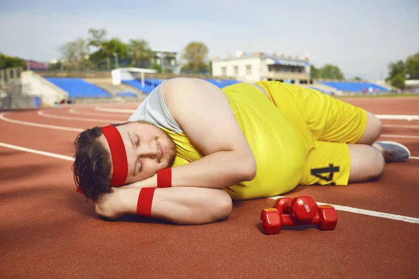 Fat lazy man sleeps tired lies on the track in the stadium.