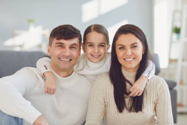 Mutlu gülümseyen aile. Kız anne ve baba gülümsüyor. Evdeki bir odada neşeli bir şekilde sarılıyorlar..