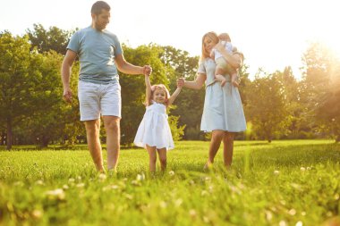 Mutlu bir aile yaz parkında çimlerin üzerinde yürüyor. Çocuk Koruma Günü.