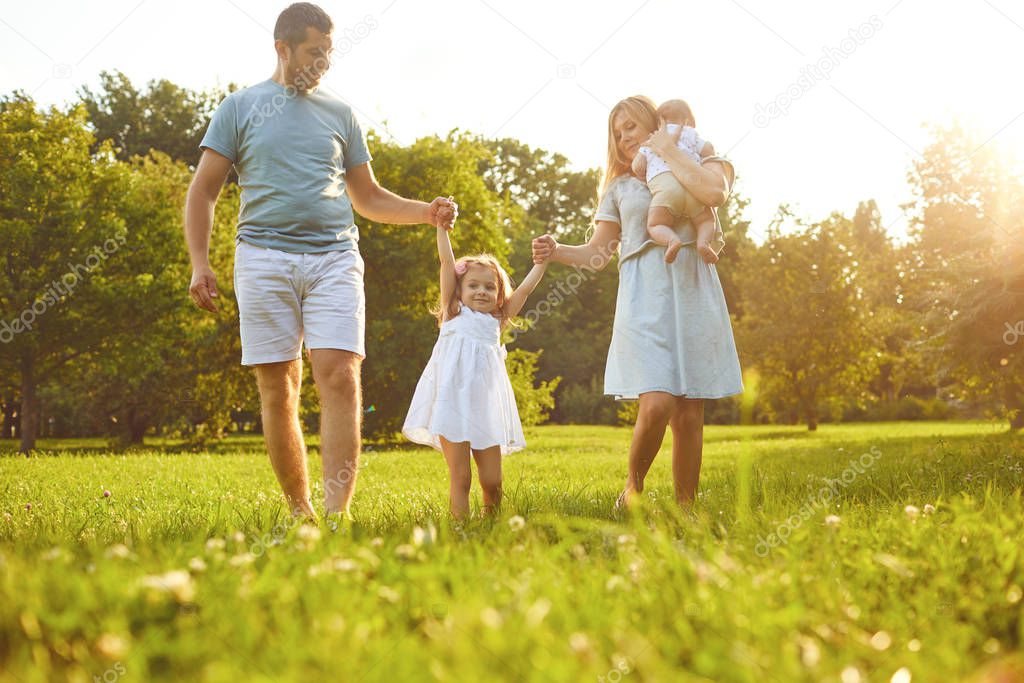 Happy family walking on the grass in the summer park. Children Protection Day.