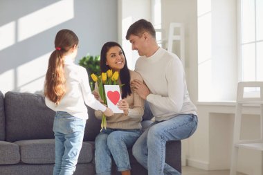 Anneler Günün kutlu olsun. Baba ve kız çocuğu, anneyi çiçeklerle ve bir odada kartpostalla kutluyor.