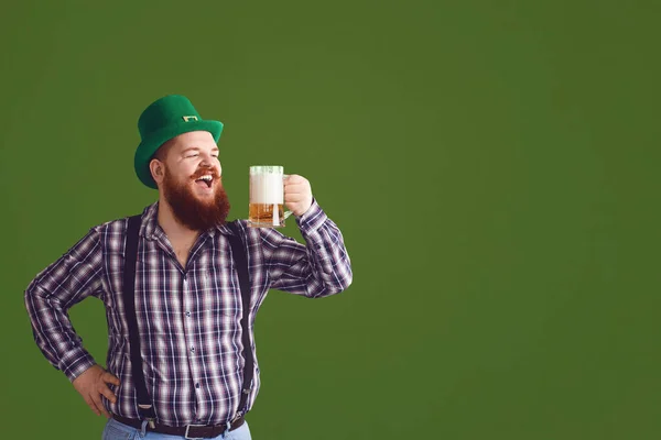 Feliz dia de St. Patricks. Gordo em um chapéu verde mantém as mãos erguidas óculos com cerveja — Fotografia de Stock