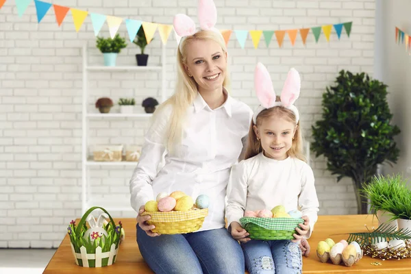 Счастливой Пасхи. Дочь и мать с кроличьими ушами украшают пасхальные яйца, сидя за столом — стоковое фото