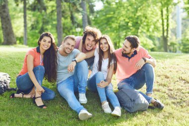 Bir şehir parkında çim üzerinde oturan arkadaşlar eğlenceli