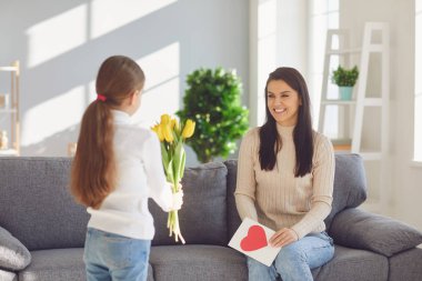 Happy mothers day. Child congratulates mom with flowers and a postcard in a room