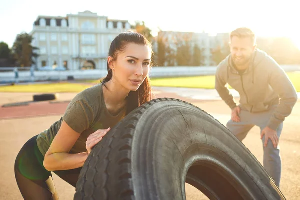 Sporty woman pushes a tire in the stadium at sunset. — Stock fotografie