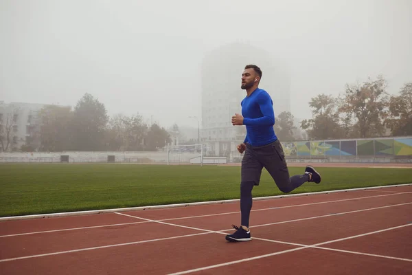 Un joven atleta corre en un estadio en la niebla . — Foto de Stock