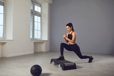 Çömelme egzersizleri. Elinde dambıllarla bir odada çömelme yapan siyah spor giysili bir kız..