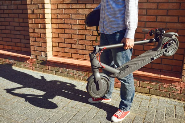 Молодой человек с электрическим скутером в руке на городской улице летом — стоковое фото