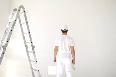 Beyaz üniformalı bir erkek ressam elinde bigudiyle beyaz bir odada çalışıyor.