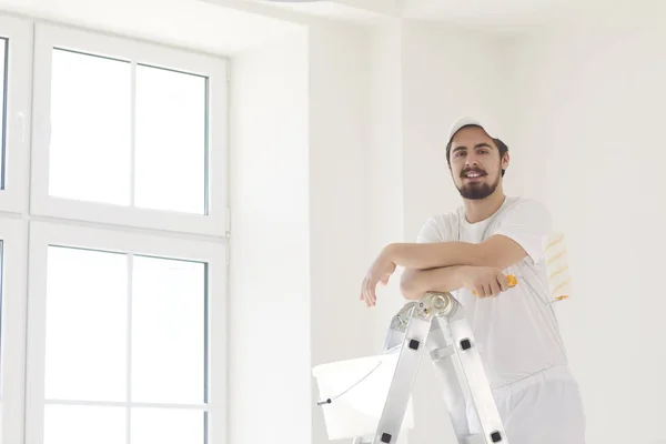 Um pintor masculino de uniforme branco com um rolo trabalha em sua mão em uma sala branca — Fotografia de Stock