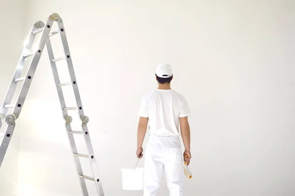 Um pintor masculino de uniforme branco com um rolo trabalha em sua mão em uma sala branca — Fotografia de Stock