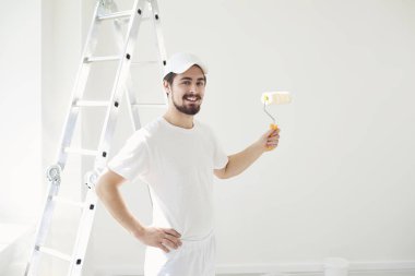 Beyaz üniformalı bir erkek ressam elinde bigudiyle beyaz bir odada çalışıyor.