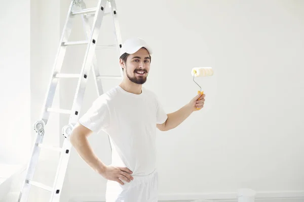 Ein männlicher Maler in weißer Uniform mit Walze in der Hand arbeitet in einem weißen Raum — Stockfoto