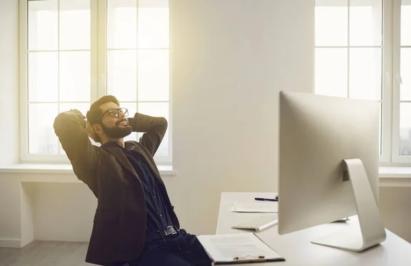 Empresário em copos mãos atrás da cabeça sonhos satisfeitos feliz sorrindo sentado a uma mesa no escritório . — Fotografia de Stock