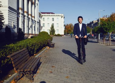 Genç hippi yazın bir şehir caddesinde elektrikli scooter kullanıyor.