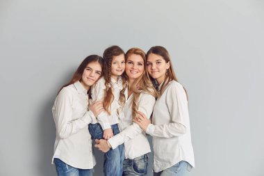 Mutlu gülümseyen anne ve kızları gri bir arka planda duruyor..