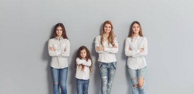 Mutlu gülümseyen anne ve kızları gri bir arka planda duruyor..