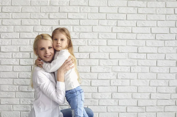 Feliz dia das mães. Mãe e filha abraçando sorrindo em um fundo de tijolo branco . — Fotografia de Stock