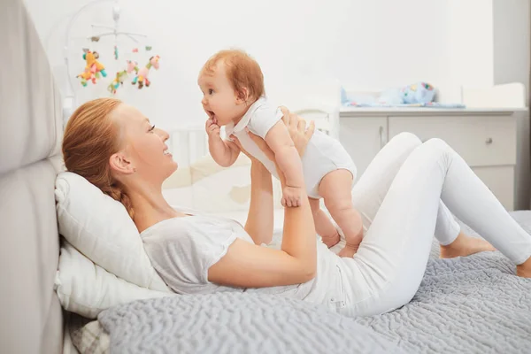 Feliz madre en bebé jugar en la cama — Foto de Stock