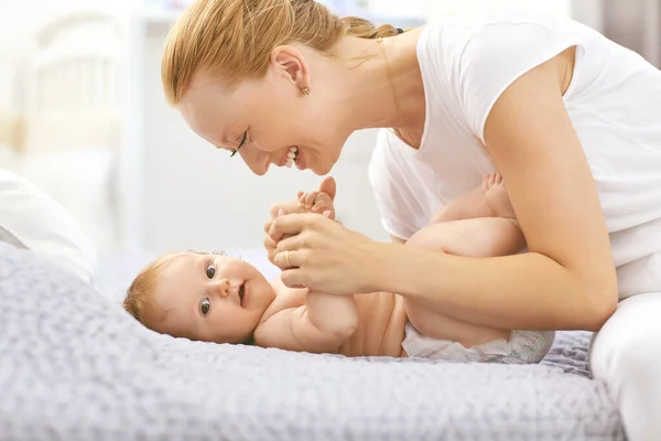 Feliz madre sonríe al bebé acostado en la cama en la habitación . — Foto de Stock