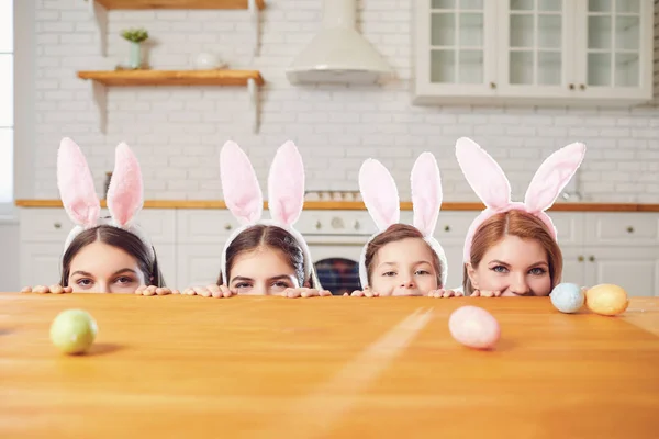 Feliz Pascua. La mamá y las hijas con las orejas de conejo adornan los huevos de Pascua a la mesa en la cocina . —  Fotos de Stock