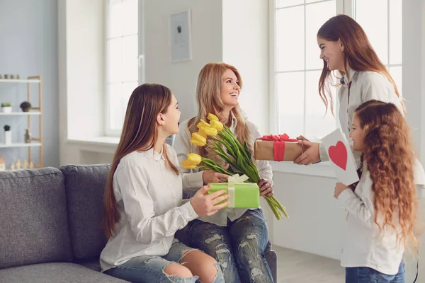 Szczęśliwego Dnia Matki. Córki dzieci dają mamie bukiet kwiatów w domu. — Zdjęcie stockowe