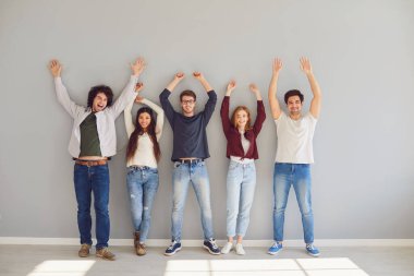 Gündelik giysiler içinde genç öğrencilerden oluşan bir grup gri bir arka plana karşı durarak ellerini kaldırıyor..