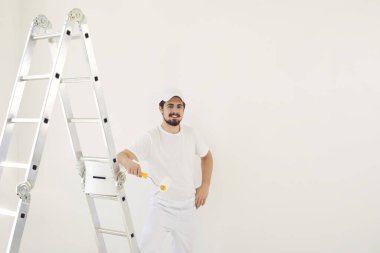 Beyaz üniformalı bir erkek ressam elinde bigudiyle beyaz bir odada çalışıyor.