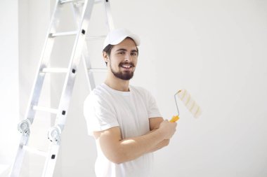 Beyaz üniformalı bir erkek ressam elinde bigudiyle beyaz bir odada çalışıyor.