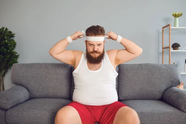 Engraçado homem gordo em sportswear está sentado no sofá na sala — Fotografia de Stock