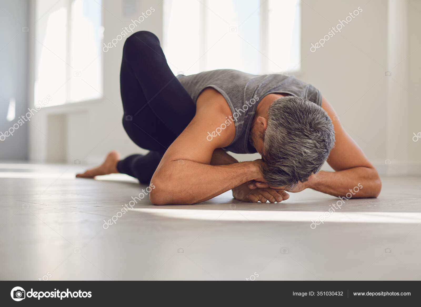 Homem do ioga. Um homem está praticando equilíbrio de ioga em uma sala  cinza . fotos, imagens de © lacheev #351030432