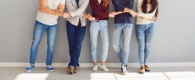 Bir grup insan gri bir duvarın arkasında dururken el ele tutuşuyorlar..