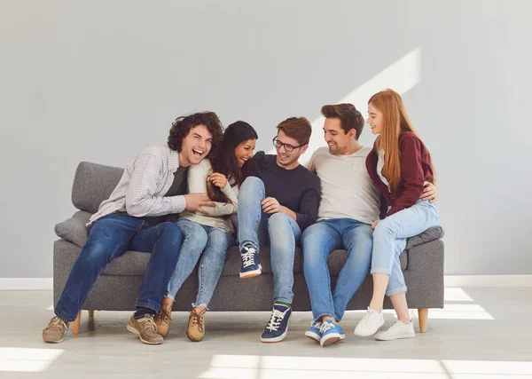 Een groep vrienden zit op de bank in een kamer op een grijze achtergrond. — Stockfoto